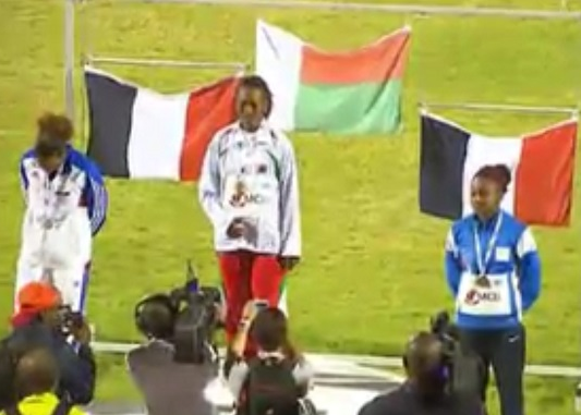 Nasrane Bacar décroche le bronze au 100m, devant un drapeau français (capture d'écran de Réunion 1ère)